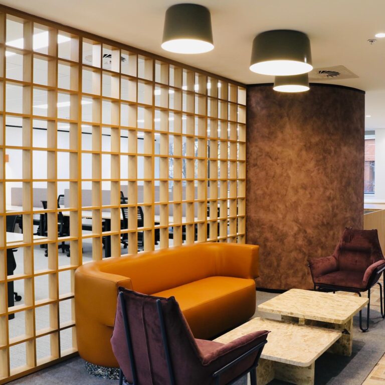 Modern office lounge area with a wooden partition, orange sofa, and burgundy chairs, showcasing a stylish commercial fitout by C&C Painting Group in Canberra City.