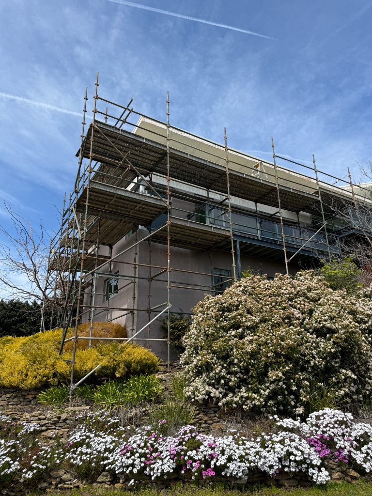 Scaffolding around a residential building surrounded by colorful flowers, illustrating C&C Painting Group's exterior project services in Canberra.