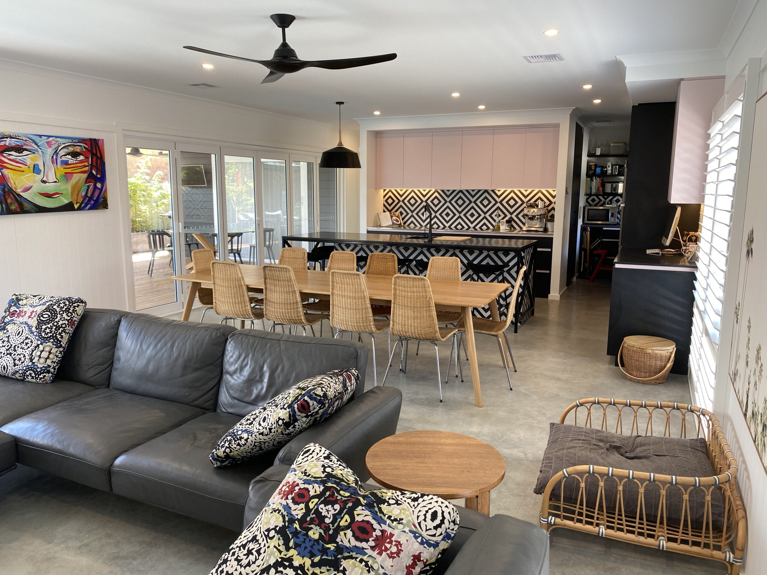 Modern open-plan living space featuring a stylish kitchen with patterned backsplash, dining table, and comfortable lounge area with decorative cushions, showcasing a vibrant artwork on the wall, ideal for new home aesthetics in Queanbeyan.