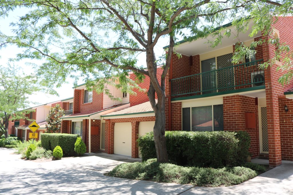 Exterior view of a strata unit complex in Monash, featuring brick buildings, green foliage, and well-maintained landscaping, illustrating C&C Painting Group's exterior repainting services.