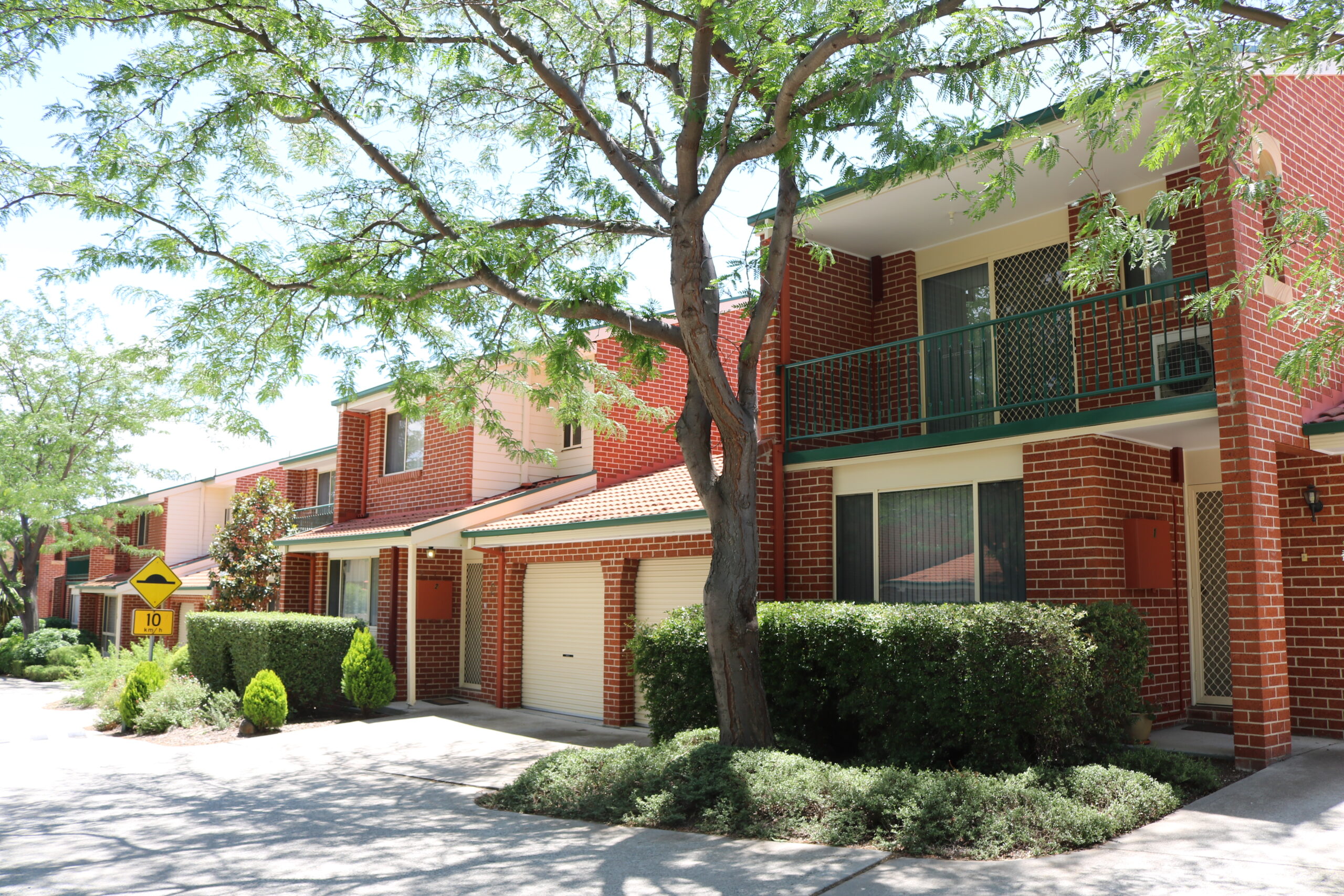 Exterior view of a strata unit complex in Monash, showcasing red brick buildings, green balconies, and landscaped gardens, highlighting C&C Painting Group's repainting services for improved aesthetics.