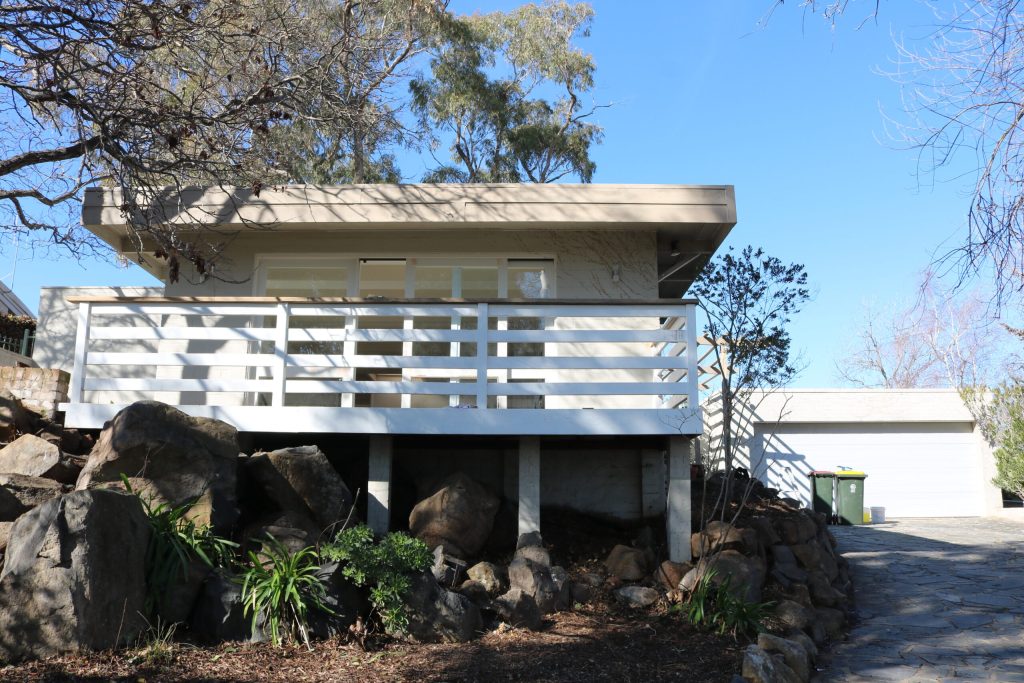 Exterior view of a modern home with a raised deck, surrounded by rocks and greenery, showcasing recent repainting work by C&C Painting Group, highlighting their expertise in home repaints in Kambah.