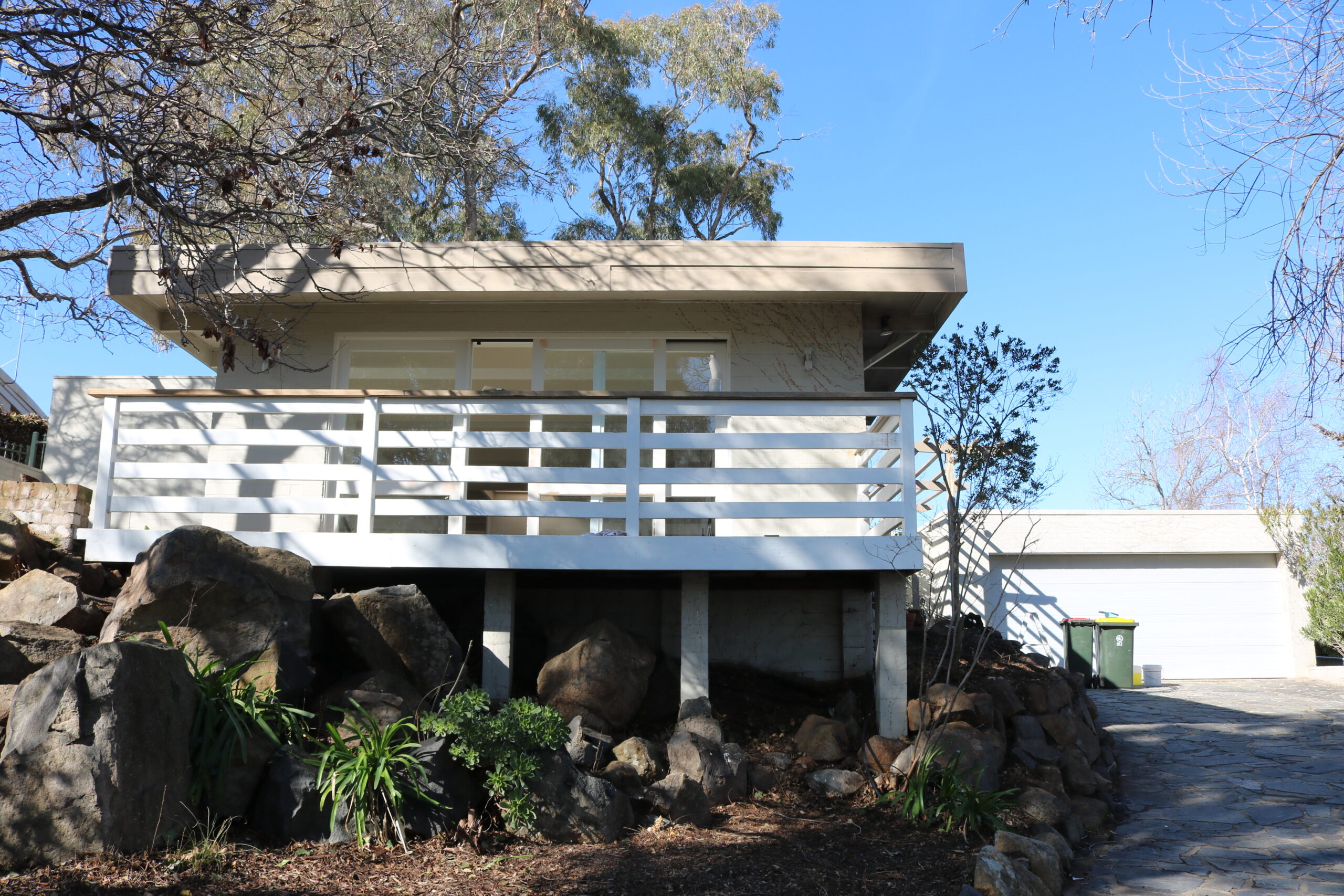 Modern home exterior with a wooden balcony, surrounded by rocks and greenery, showcasing C&C Painting Group's expertise in home repaint services in Fadden.