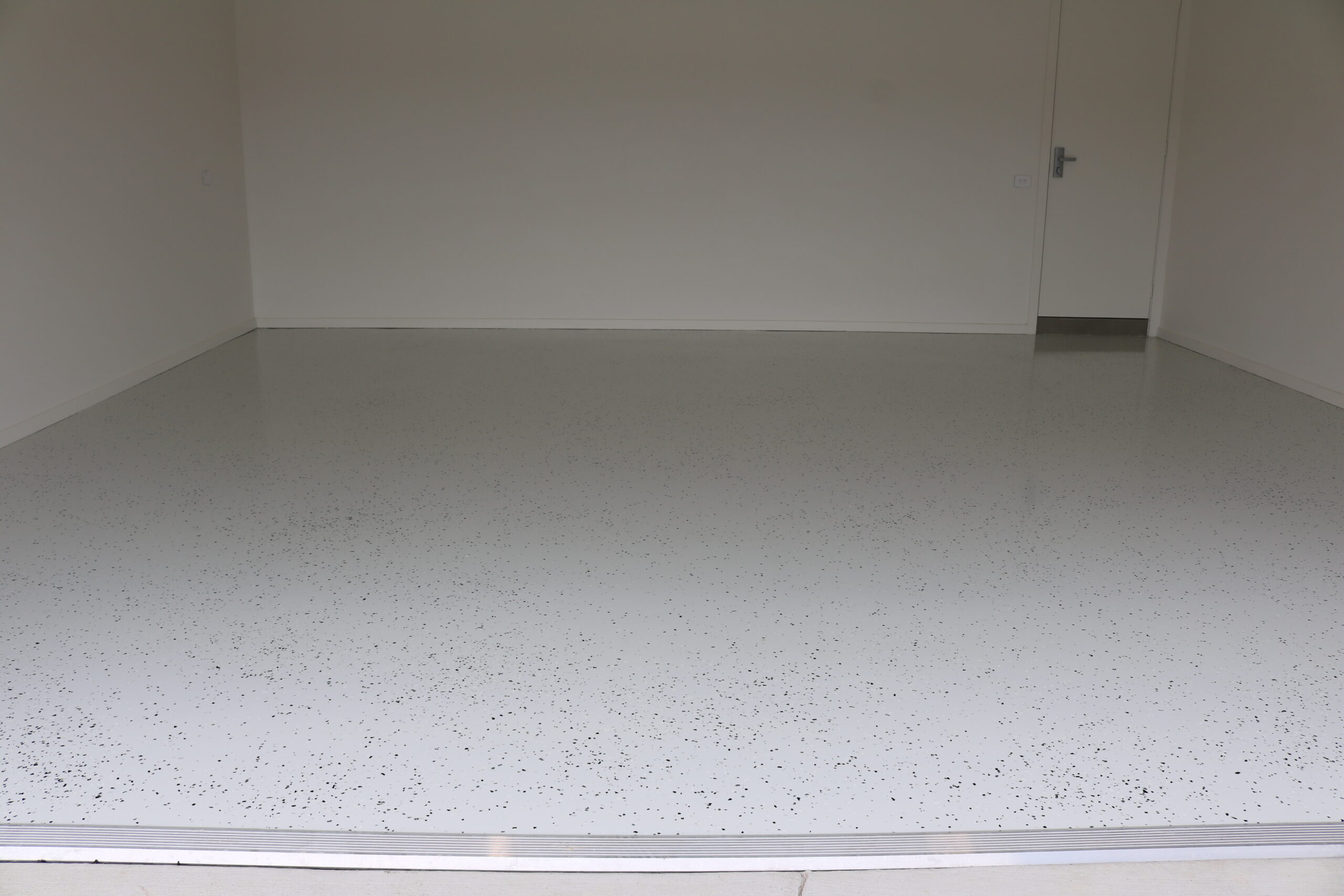 Decorative concrete garage floor with white base and black speckles, showcasing resurfacing quality by C&C Painting Group.