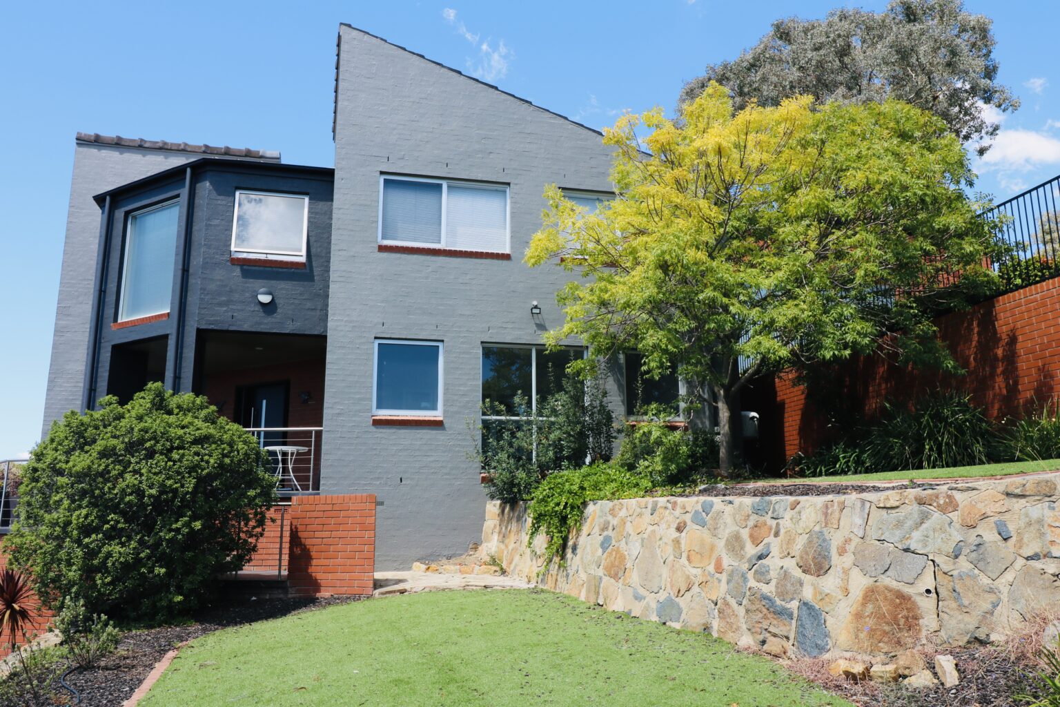 Exterior of a modern home in Calwell, Canberra, showcasing a fresh grey repaint, landscaped garden with greenery, and stone wall features, highlighting C&C Painting Group's exterior residential painting services.