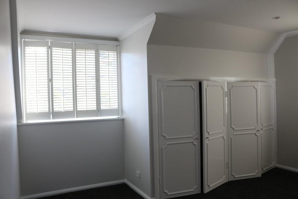 Interior of a freshly painted room in Chapman, featuring white walls, a window with shutters, and a closet with decorative doors.