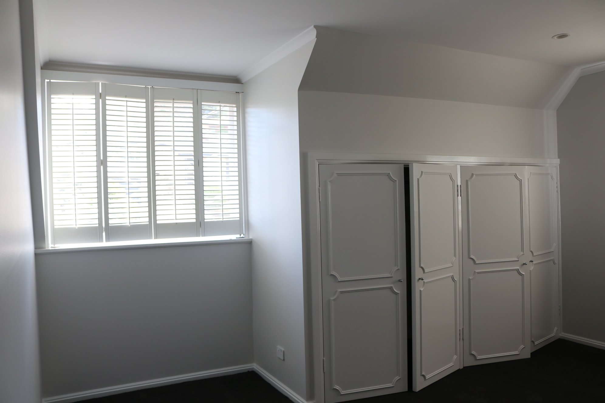 Interior of a freshly painted room in Chapman, featuring white walls, a window with blinds, and a built-in wardrobe with white doors.