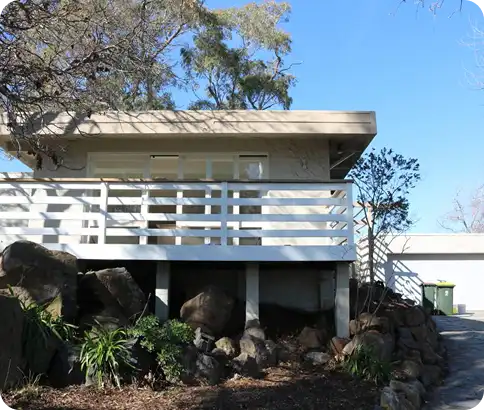 Modern home exterior with a balcony, surrounded by natural landscaping and large rocks, showcasing a clean and well-maintained appearance, reflecting C&C Painting Group's commitment to quality and aesthetic enhancement in residential repainting.