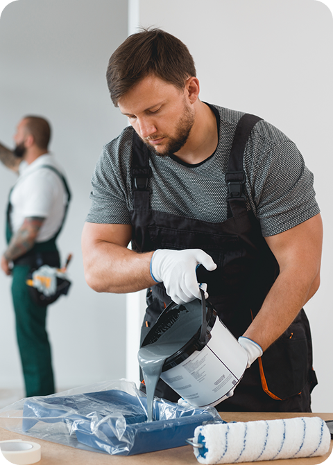 Professional painter pouring paint into a tray, showcasing skilled craftsmanship and attention to detail, with a second tradesman preparing in the background, reflecting C&C Painting Group's commitment to quality painting services in Canberra.