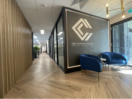 Modern office interior of C&C Painting Group featuring logo wall, stylish blue chairs, and wooden paneling, reflecting a commitment to quality and professionalism.
