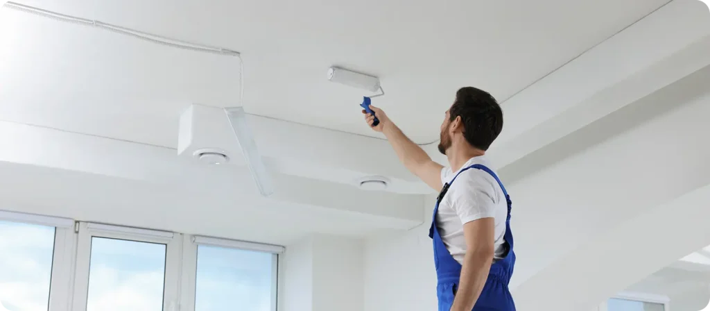 Painter using a roller to apply paint on a ceiling in a well-lit interior space, illustrating quality workmanship and professionalism at C&C Painting Group.