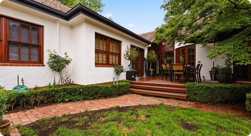 Residential home exterior with modern and heritage design elements, showcasing freshly painted white walls, wooden windows, and a landscaped garden with brick pathways and patio furniture, highlighting the benefits of professional repainting services by C&C Painting Group in Canberra.