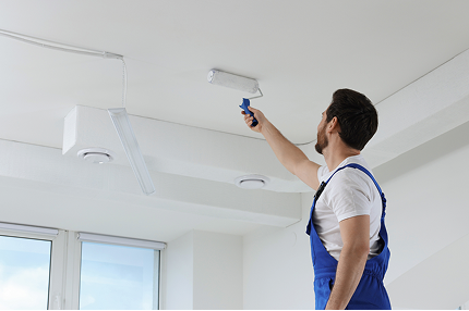 Man painting a ceiling with a roller in a modern interior, representing quality workmanship at C&C Painting Group.