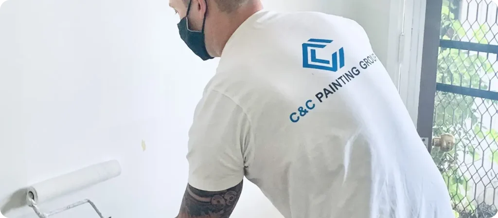 Painter from C&C Painting Group applying paint with roller in residential setting, showcasing professional workmanship and team branding.