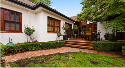 Residential home exterior with freshly painted white walls, wooden window frames, and a landscaped garden, showcasing a deck area with outdoor furniture, emphasising C&C Painting Group's residential repainting services in Canberra.