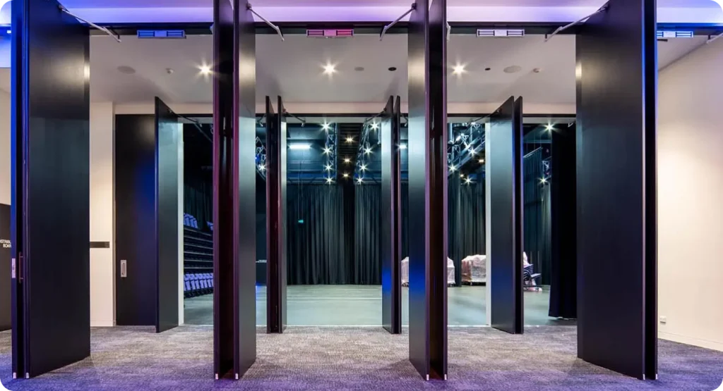 Interior view of a modern commercial space featuring multiple black folding doors, leading to a stage area with theatrical lighting, designed for government and commercial events.