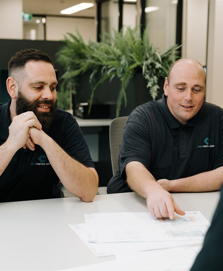 Two C&C Painting Group team members discussing project plans at a table, showcasing collaboration in property services and project management.