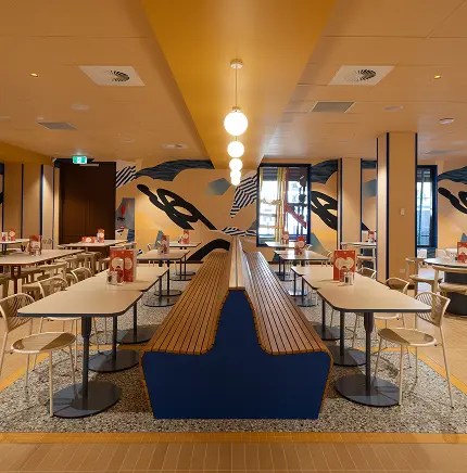 Modern café interior featuring wooden benches, contemporary tables, and colourful wall art, reflecting a vibrant atmosphere suitable for commercial dining spaces.
