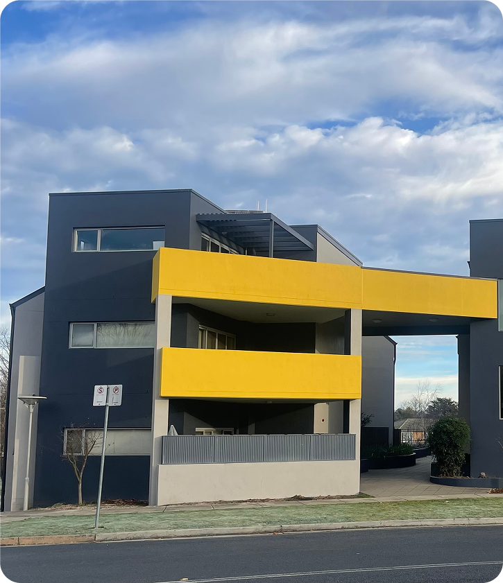 Modern strata apartment building with bold yellow accents and grey exterior, showcasing quality painting and maintenance work by C&C Painting Group in Canberra.