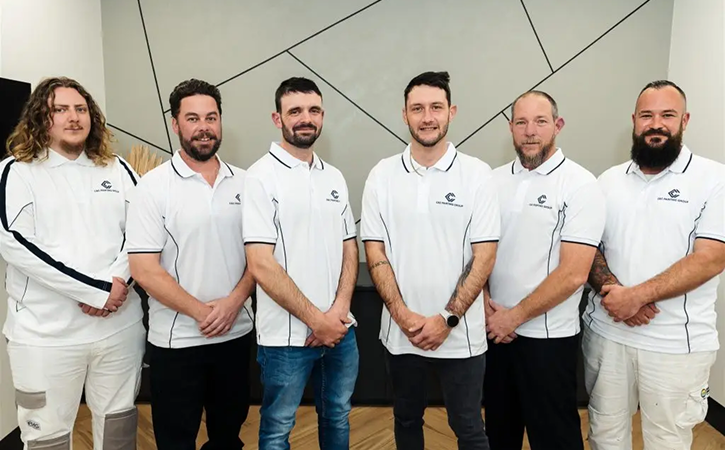 Team of professional painters from C&C Painting Group, wearing branded polo shirts, standing together in a modern interior setting, showcasing commitment to quality service and customer satisfaction in residential repainting.