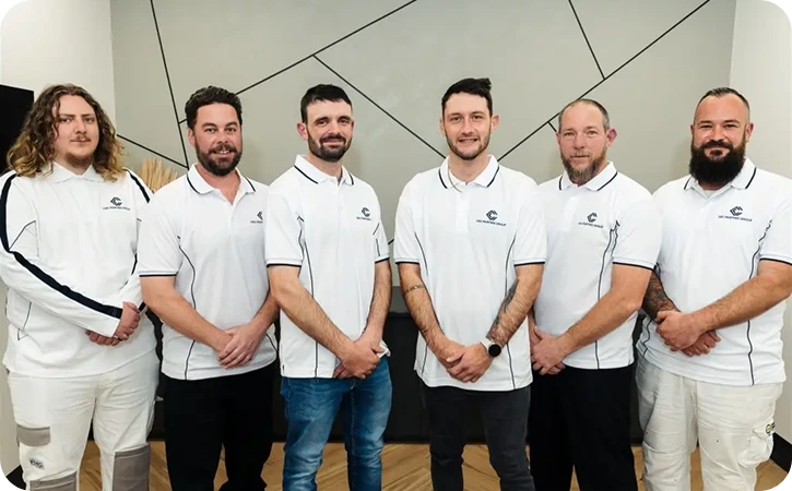 Team of professional painters from C&C Painting Group, dressed in branded polo shirts, standing together in a modern interior setting, showcasing their commitment to quality residential repainting services in Canberra.