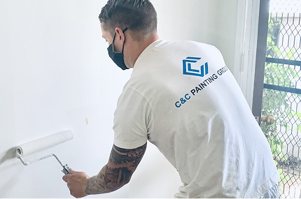 Painter from C&C Painting Group applying paint with a roller on a wall, showcasing professional painting services in a residential setting.