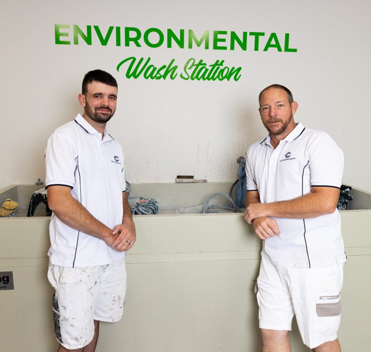 Two professional painters standing beside an environmental wash station, featuring the text "ENVIRONMENTAL Wash Station" in green, showcasing C&C Painting Group's commitment to eco-friendly practices in their painting services.