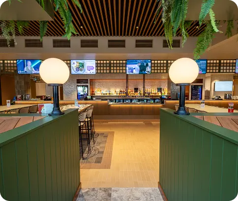 Interior view of a modern bar featuring green panelled counters, round lamps, and multiple screens displaying information, showcasing C&C Painting Group's high-quality finishes in commercial environments.