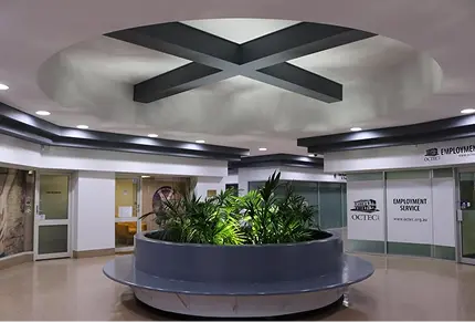 Interior of a commercial space featuring a circular planter with lush greenery, modern ceiling design with intersecting beams, and signage for employment services, reflecting professional and compliant design suitable for government and commercial environments.