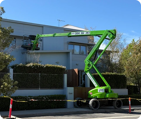 Green cherry picker lift positioned outside a modern building, facilitating access for maintenance and painting services, surrounded by safety barriers.