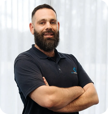 Man with beard wearing a C&C Painting Group polo shirt, standing confidently with arms crossed, in a well-lit office environment, representing the company's commitment to quality service and team expertise.