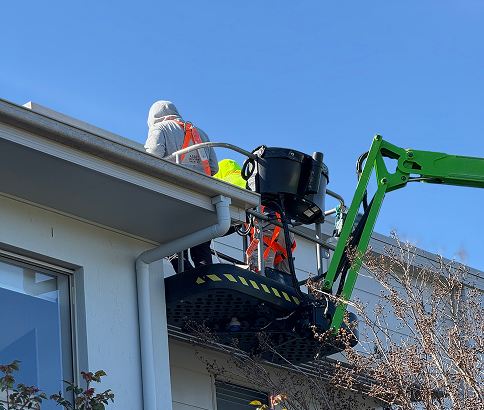 Workers in safety gear using a platform lift to perform maintenance on a building's exterior, emphasising proactive property management and professional painting services for strata properties.