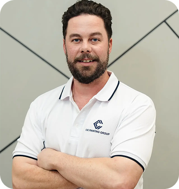 Team leader from C&C Painting Group in a white polo shirt, smiling confidently with arms crossed, showcasing professionalism and expertise in painting services.