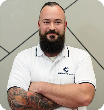 C&C Painting Group team member with a beard and tattoos, wearing a branded polo shirt, standing confidently against a geometric background.