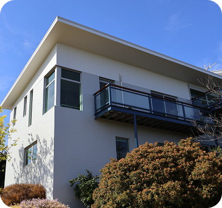 Modern residential building with a balcony, surrounded by landscaped greenery, showcasing quality painting and finishing services by C&C Painting Group in Canberra.