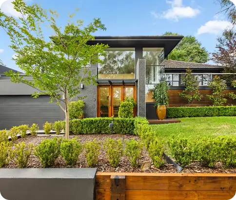 Modern home exterior with landscaped garden, featuring a glass entrance, wooden accents, and greenery, showcasing C&C Painting Group's residential repainting expertise.