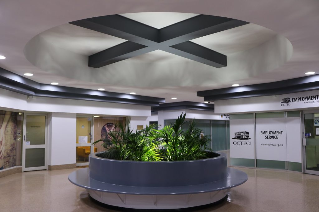 Interior view of a modern commercial space featuring a circular planter with greenery, unique ceiling design with geometric patterns, and signage for OCTEC Employment Service, showcasing C&C Painting Group's expertise in commercial painting projects.