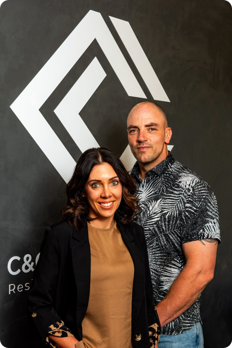 Two professionals posing confidently in front of a modern C&C Painting Group logo, showcasing commitment to quality and teamwork in the painting industry.