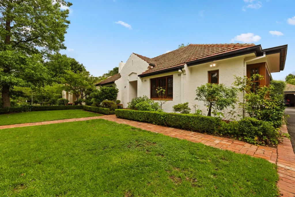 Residential exterior of a well-maintained home in Queanbeyan, showcasing quality landscaping with manicured lawns and brick pathways, emphasizing C&C Painting Group's professional repainting services and commitment to high-quality finishes.