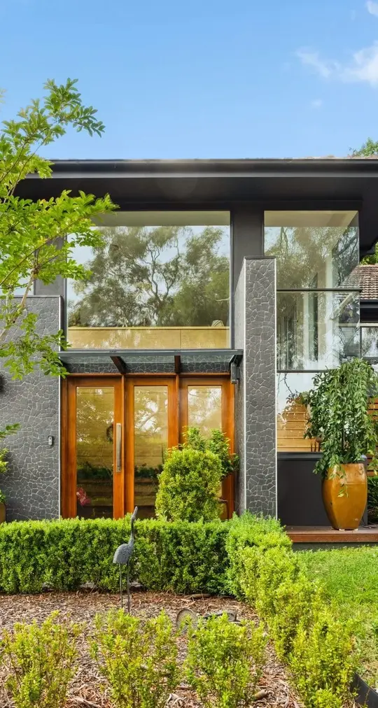 Modern residential exterior showcasing a stylish entrance with wooden doors, surrounded by lush greenery and decorative planters, reflecting C&C Painting Group's expertise in enhancing home aesthetics in Queanbeyan.