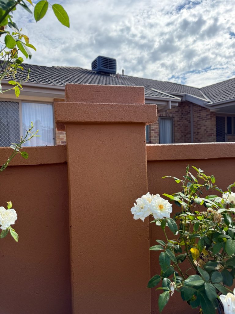 Freshly painted fence post with white flowers and a residential backdrop, showcasing quality exterior improvement and landscaping.