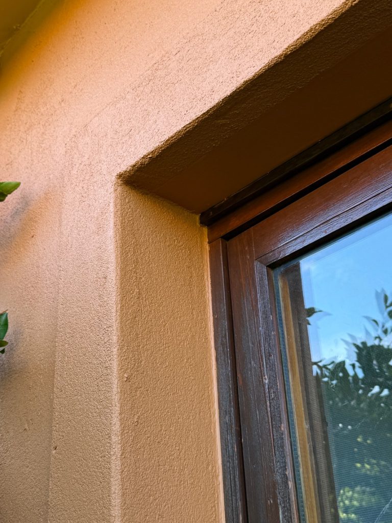Close-up of freshly rendered and painted window corner with textured wall and wooden frame, showcasing quality craftsmanship and attention to detail in property improvement by C&C Painting Group.