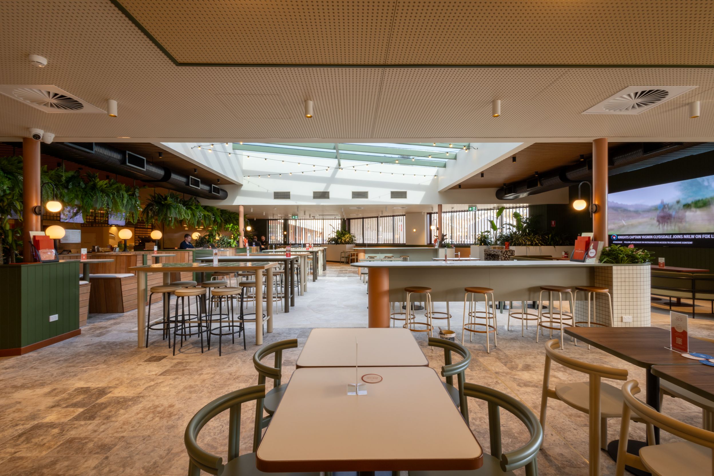 Interior view of the Canberra Southern Cross Club, featuring modern seating arrangements, a bar area, and abundant greenery, showcasing the quality of the commercial painting project by C&C Painting Group.