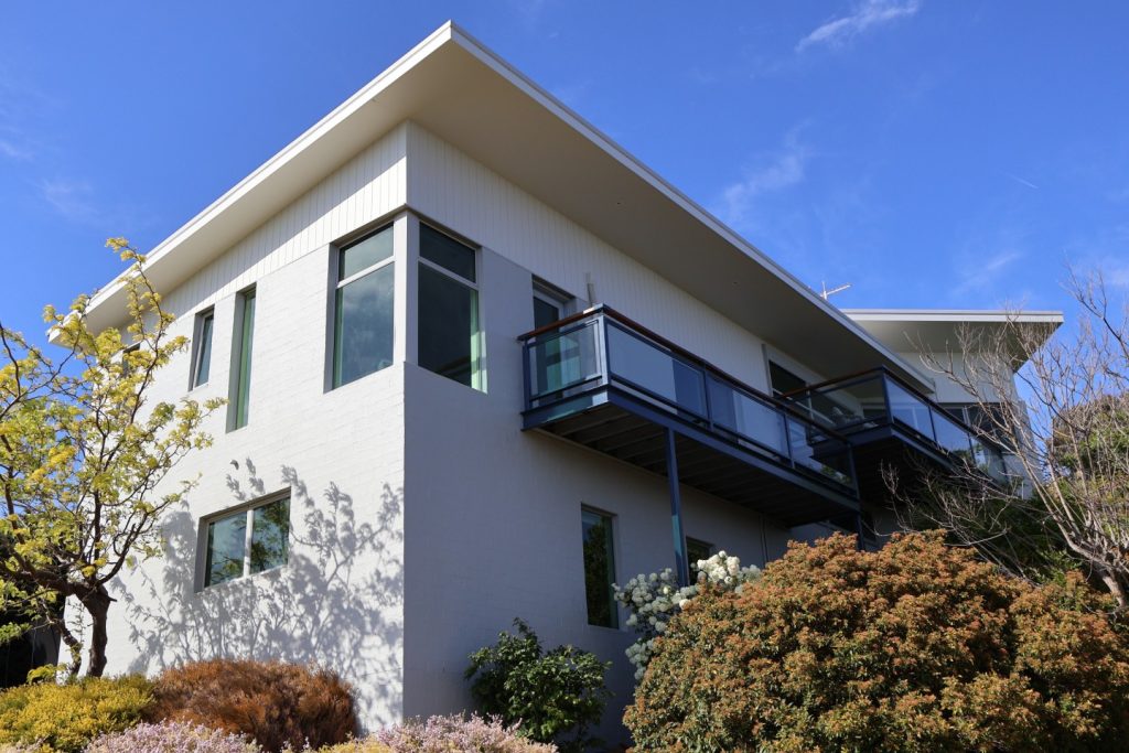 Modern residential building with large windows and balcony, surrounded by landscaped gardens, illustrating C&C Painting Group's property services.