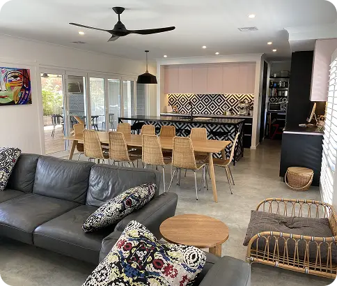 Modern interior of a Canberra home featuring a stylish living area with a gray sofa, decorative pillows, a round coffee table, and a dining space with a long table and wicker chairs, showcasing contemporary design elements and an open layout.