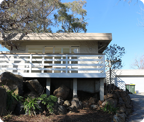 Residential home exterior in Queanbeyan with a white railing, surrounded by rocks and greenery, showcasing a well-maintained appearance, emphasizing quality residential painting services.