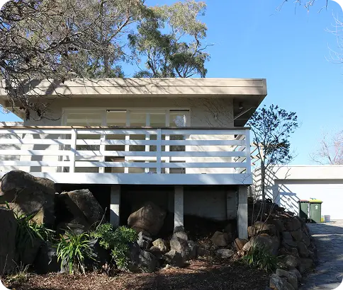 Modern residential home in Canberra with a white balcony, surrounded by rocks and greenery, showcasing professional repainting quality and exterior transformation.