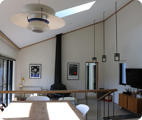 Modern interior of a residential space featuring a wooden dining table, contemporary lighting fixtures, a black fireplace, and large windows, showcasing a bright and inviting atmosphere, reflecting C&C Painting Group's focus on quality home transformations in Queanbeyan.