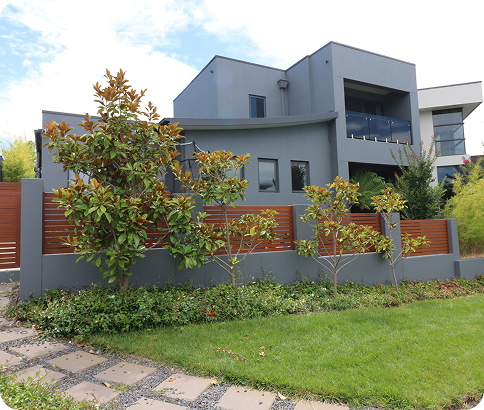 Modern residential home exterior with landscaped garden, featuring grey walls, wooden fencing, and decorative trees, showcasing quality painting and design in Queanbeyan.