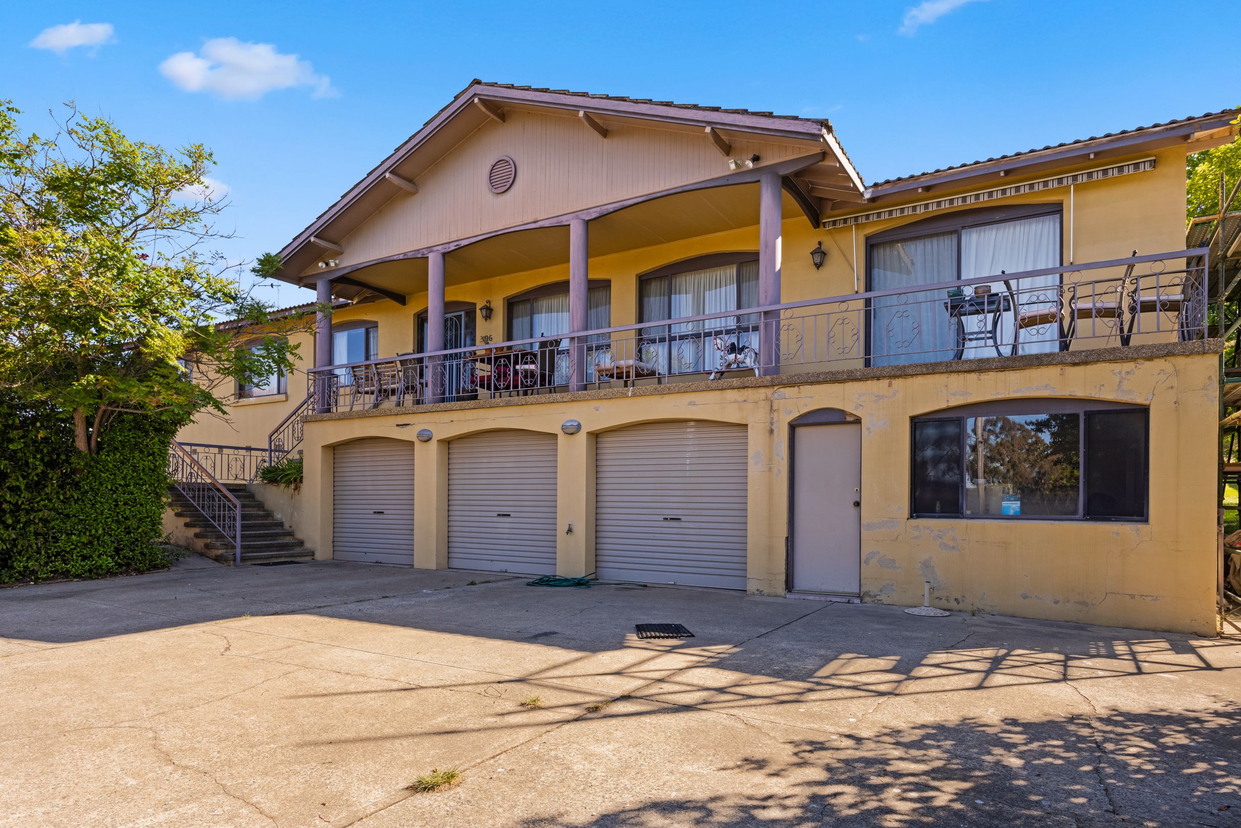 Residential home in Queanbeyan featuring a yellow exterior, balcony with seating, and garage doors, illustrating potential before and after repainting transformation by C&C Painting Group.